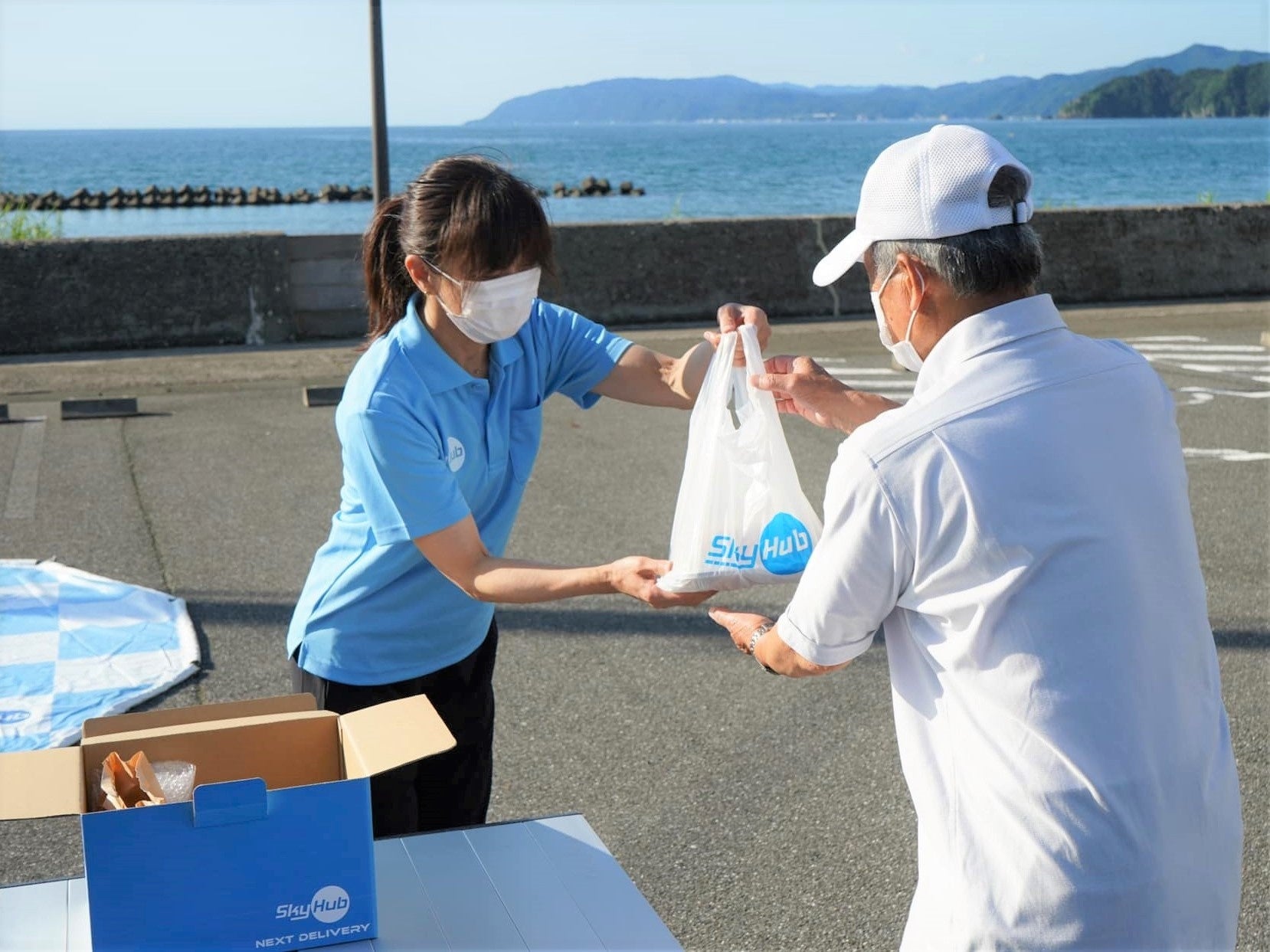 ドローン配送されたテイクアウト商品をスタッフから受取る植本太郎さん（東浦公民館前）