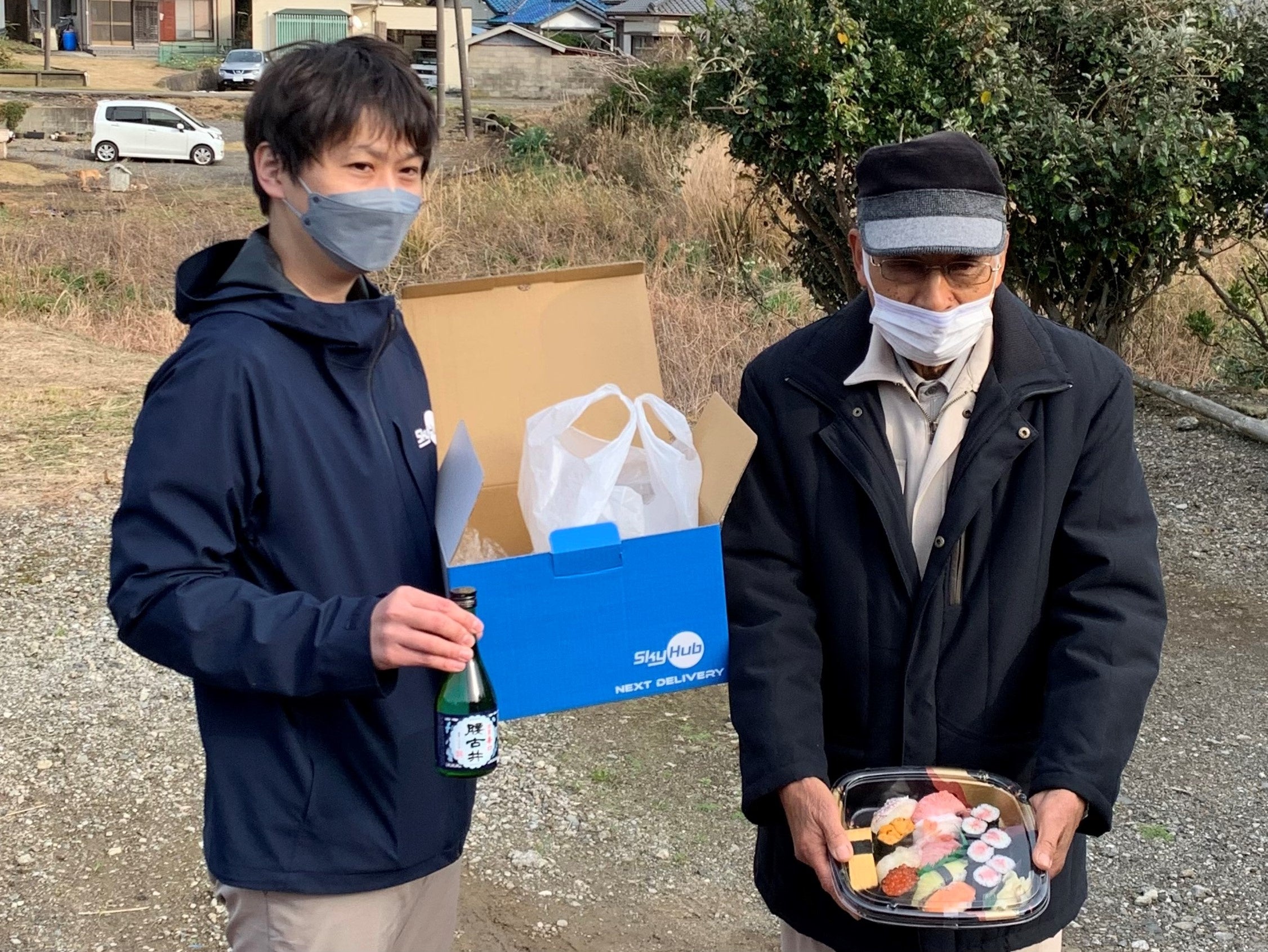 ドローン配送された「晩酌セット」のにぎり鮨が崩れていないことを見せる受け取った鈴木恒夫大沢区長